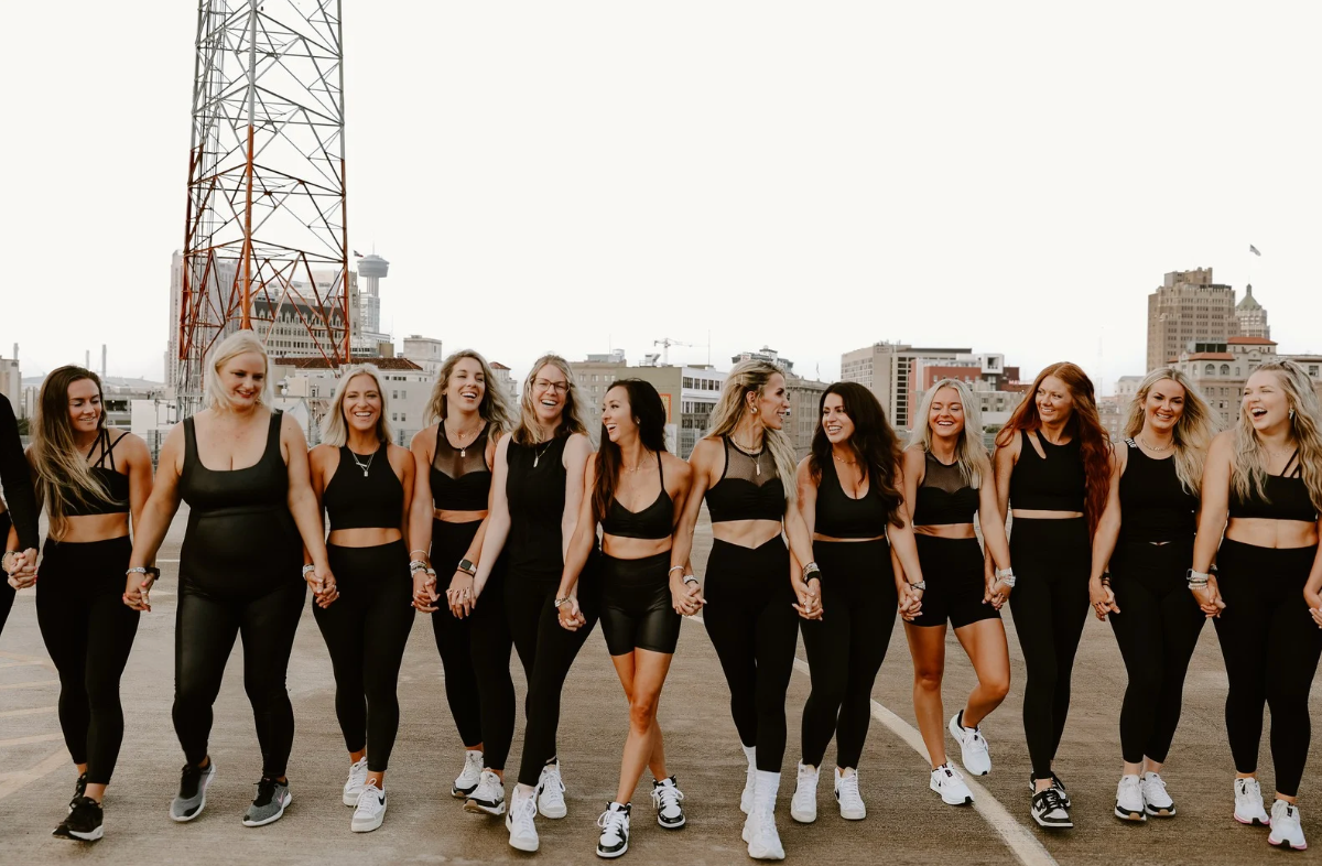 Group of women in workout gear holding hands.